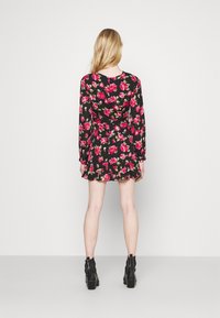 Musta pitkähihaisen mekko, jossa on kukkakuosi, joka sisältää punaisia ja vihreitä ruusuja, liehuva helma ja vartalonmyötäinen siluetti. Mallilla on päällään mustat nilkkurit.