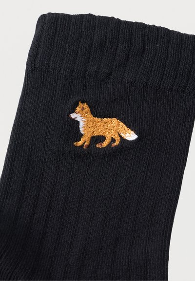 Μαύρη ριγωτή κάλτσα με μια μικρή κεντημένη πορτοκαλί αλεπού με λευκές λεπτομέρειες που κοιτάζει προς τα αριστερά κοντά στη μανσέτα.