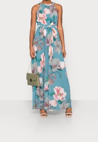 Robe maxi en tissu teal avec un motif floral rose et vert. Présente un col haut, des bretelles halter et une taille cintrée.