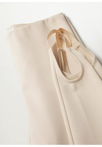 Haut beige sans manches plié avec de fines bretelles élastiques sur une surface blanche.