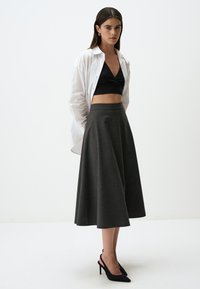 Zwarte crop top, witte blouse met knopen, en een donkergrijze gescheurde rok van een zachte stof; gecombineerd met zwarte hoge hakken.