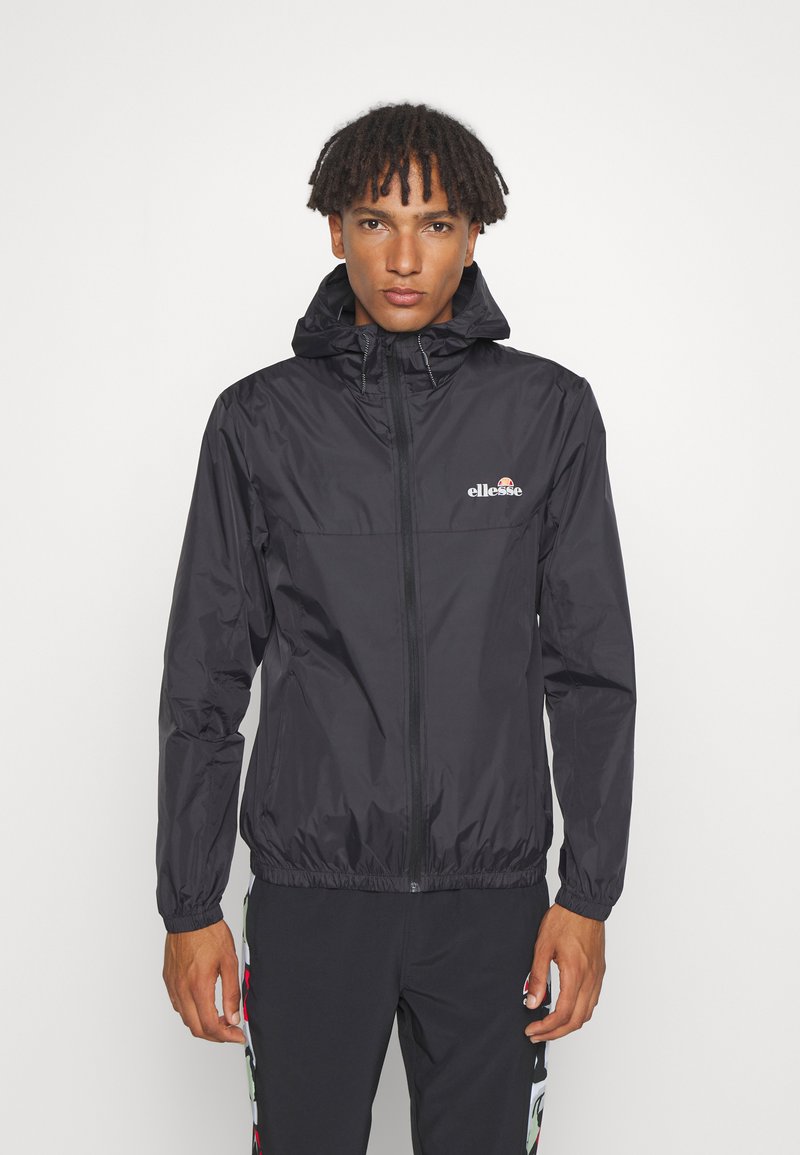 Schwarze, leichte Jacke mit Kapuze, ausgestattet mit elastischen Bündchen und einem Reißverschluss vorne. Auffälliges Logo auf der Brust. Glattes, wasserabweisendes Material.