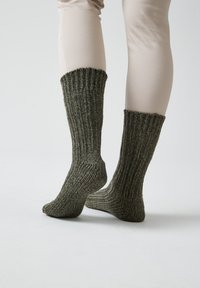Calze di lana alte fino al ginocchio di colore verde scuro, con una texture a coste e un tessuto spesso e caldo. Il design include un risvolto nella parte superiore.