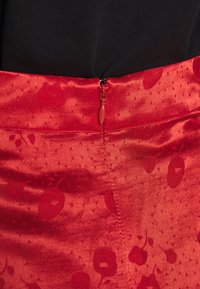 Tissu en satin rouge avec des motifs subtils de cerises et une fermeture éclair fermée sur fond noir.