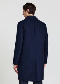 Cappotto in lana blu navy con design lungo, ampio colletto e dettaglio di spacco posteriore, con tessuto liscio e vestibilità sartoriale.