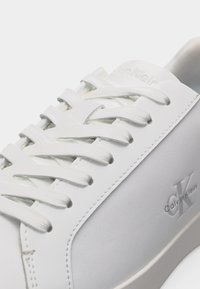 Λευκό αθλητικό παπούτσι Calvin Klein με λευκά κορδόνια, ορατή ραφή και ανάγλυφο λογότυπο στο πλάι.