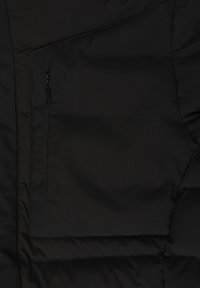 Juodas pamuštas džemperis su užtrauktuku, sklandžiu tekstūru, matinio paviršiaus ir siūle, kur susijungia audinio plokštės.