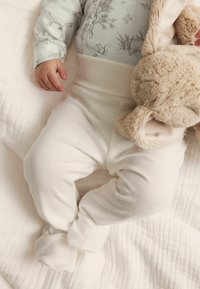 Weiße Baumwollhose für Kleinkinder im Fußdesign, mit geripptem Muster und weitem Bund, kombiniert mit einem weichen Stofftier.