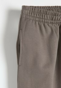 Szare dresowe spodnie wykonane z miękkiego materiału, z elastycznym paskiem w talii i bocznymi kieszeniami dla funkcjonalności. Gładka tekstura bez wzorów.