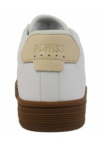 Sneaker bianca con tomaia in pelle testurizzata, linguetta sul tallone beige e suola in gomma marrone. Presenta un logo in rilievo sul retro e cuciture a contrasto.