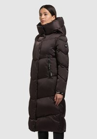 Langer Steppmantel in Dunkelbraun mit einem hohen Kragen, Reißverschlusstaschen und gesteppten Abschnitten. Hergestellt aus satinähnlichem Material mit glatter Textur.