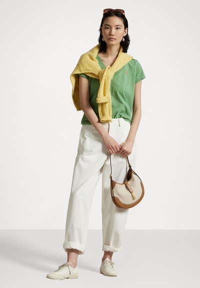Green cotton T-shirt with a small logo, yellow knitted sweater draped over shoulders, white cuffed trousers, and a beige shoulder bag with brown accents.