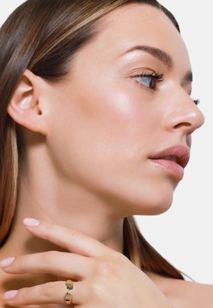Goldfarbener Schmuckring mit Handdesign, strukturierter Oberfläche, auf der Haut eines Models platziert. Haare glatt gestylt, mit dezentem Make-up.