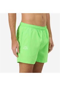 Costumi da bagno verde brillante con vita elastica, tasca laterale e dettaglio logo bianco sulla coscia sinistra. Texture liscia e design casual.
