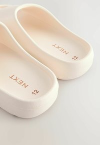 Helle rosa Gummi-Clogs mit strukturierter Oberfläche, ausgestattet mit einem breiten Riemen und geprägtem Logo, Größe 12. Glatte Innenfläche.
