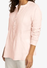 Blouse rose clair en tissu léger, dotée d'une patte de boutonnage, d'un devant plissé et de manches longues avec des bords côtelés.