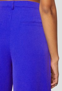 Pantalons violets en tissu lisse, dotés d'une taille mi-haute, de deux poches arrière et d'une coupe ajustée.