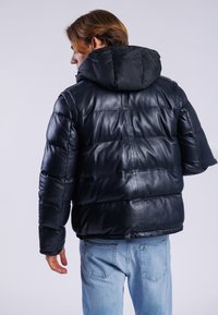 Sort læder pufferjakke med hætte, der har en quiltet struktur og en let løs pasform, parret med lyseblå jeans.