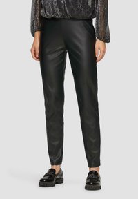 Zwarte neplederen broek met een slim fit, met een gladde textuur en een licht glanzend oppervlak. Gecombineerd met glanzende zwarte schoenen.
