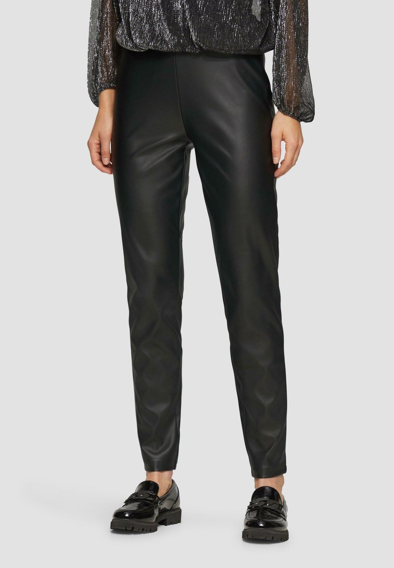 Zwarte neplederen broek met een slim fit, met een gladde textuur en een licht glanzend oppervlak. Gecombineerd met glanzende zwarte schoenen.