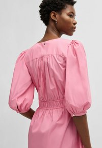 Pink cotton dress with puff sleeves, elastic waistband, and button detail at the back. Smooth texture and relaxed fit.