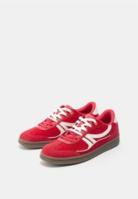 Paar rote Wildledersneaker mit weißen Streifen, weißen Schnürsenkeln und braunen Gummisohlen auf weißem Hintergrund.