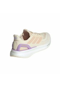 Licht beige hardloopschoen met roze accenten en een paarse hielclip. Heeft een gestructureerde bovenkant en een witte, gevoerde zool. Pureboost branding zichtbaar.
