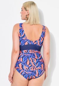 Een badpak met een veelkleurig abstract bladpatroon in roze, blauw en marineblauw, voorzien van een brede schouderband en een uitsnede op de rug.