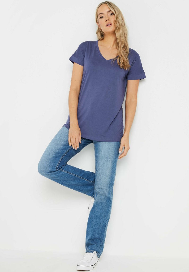 T-shirt z dekoltem w serek w kolorze granatowym, z krótkim rękawem, zestawiony z jasnoniebieskimi jeansami i białymi trampkami. Tkanina wydaje się gładka i elastyczna.