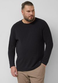 Zwart shirt met lange mouwen, een ronde hals en geribbelde manchetten, gemaakt van een getextureerde stof. Gecombineerd met lichtbeige broek.