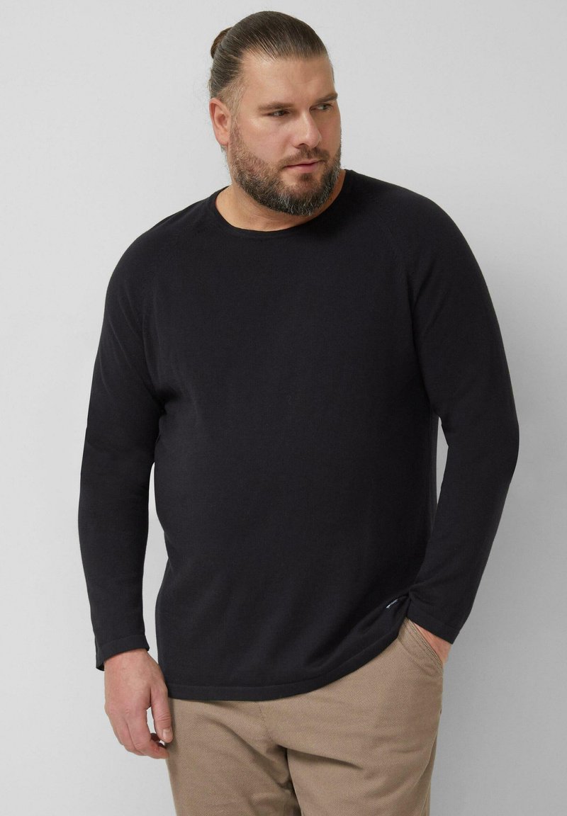 Zwart shirt met lange mouwen, een ronde hals en geribbelde manchetten, gemaakt van een getextureerde stof. Gecombineerd met lichtbeige broek.