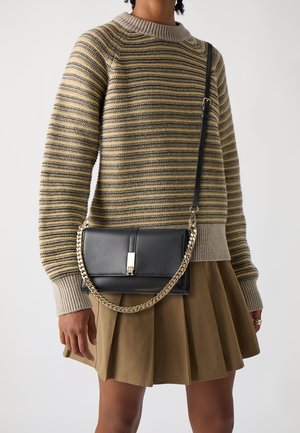 Sort lædertaske med guld kæderem og sølvhardware; slankt design med klaplukning, kombineret med en stribet sweater.