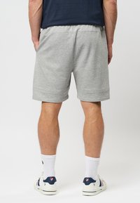 Shorts en mélange de coton gris avec une coupe décontractée, dotés d'une taille élastique et d'ourlets roulés. Portés avec des chaussettes blanches et des chaussures décontractées.