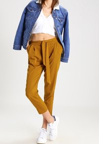 Džínová bunda s ovčím límcem, bílý zkrácený top a hořčicově žluté kalhoty tapered v pase, doplněné bílými teniskami.