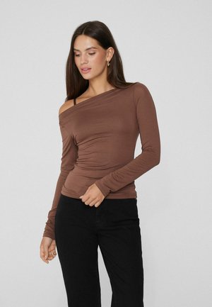 Haut marron à manches longues, décolleté épaule dénudée, avec une texture froncée, présentant une fine bretelle sur une épaule et un design ajusté, associé à un pantalon noir.