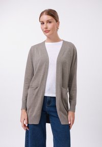 Light gray knitted cardigan with open front, two front pockets, and ribbed cuffs. Worn over a white top and paired with blue jeans.