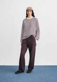 Striped long-sleeve shirt in white and burgundy, paired with burgundy pants. Black sneakers and a tan cap complete the look.