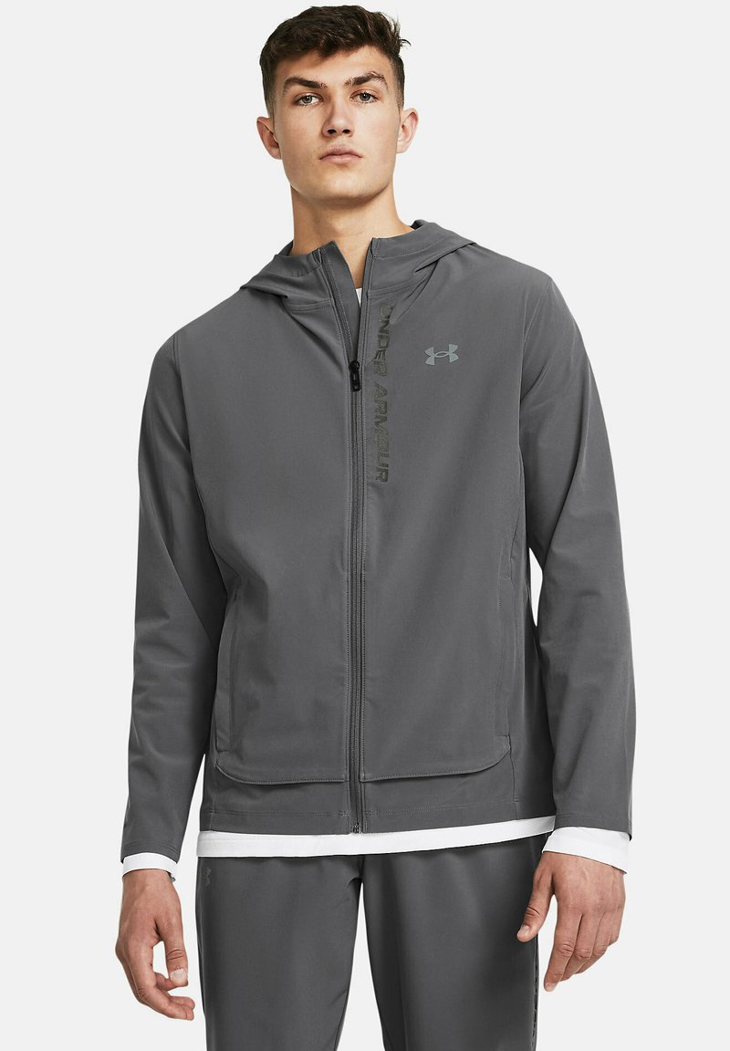 Grå zip-up hættejakke i letvægtsstof, justerbar hætte og Under Armour-logo. Har en glat overflade og afslappet pasform.