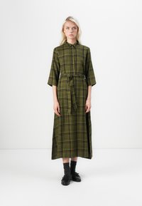 Green plaid dress with a collar, front buttons, and a tie belt. Features three-quarter sleeves and a long, flowing silhouette.