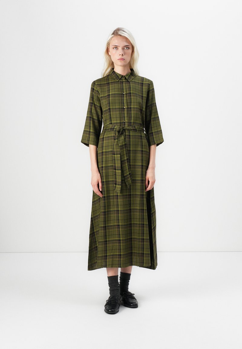 Green plaid dress with a collar, front buttons, and a tie belt. Features three-quarter sleeves and a long, flowing silhouette.