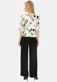 Biała bluzka z czarnym kwiatowym wzorem i dekoltem w kształcie litery V, w zestawieniu z czarnymi spodniami o szerokich nogawkach. Strój posiada rękawy do trzech czwartych i jest wykonany z miękkiego materiału.