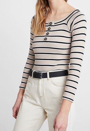 Top de manga larga con canalé y rayas horizontales en beige y negro, con un escote amplio y cierre frontal de tres botones, combinado con pantalones de talle alto.