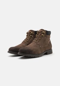 Stivali in suede marrone con occhielli in metallo, lacci marroni e un colletto nero. Presentano suola in gomma e dettagli di cucitura laterale.