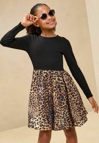 Robe noire à manches longues avec une jupe plissée en imprimé léopard. Texture douce, taches brunes et noires vives, design longueur genoux.
