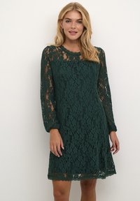 Robe en dentelle verte présentant de longues manches bouffantes, un ourlet festonné et des motifs floraux. Tissu léger avec une texture délicate.