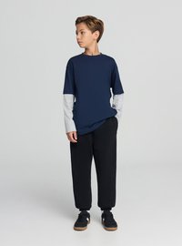 Maglietta blu navy con maniche lunghe grigio chiaro, pantaloni della tuta neri e scarpe da ginnastica nere con suole marroni. Design semplice con scollo rotondo.