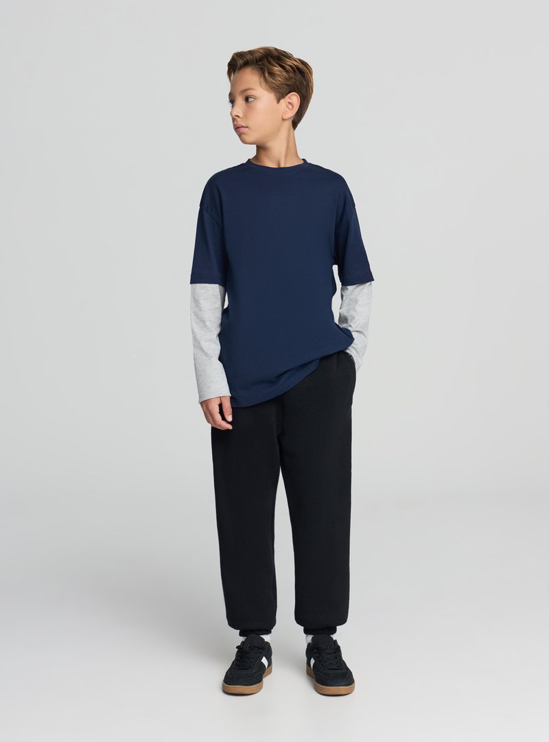 Maglietta blu navy con maniche lunghe grigio chiaro, pantaloni della tuta neri e scarpe da ginnastica nere con suole marroni. Design semplice con scollo rotondo.