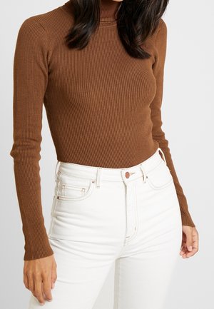 Maglione a collo alto rigato marrone con maniche lunghe, abbinato a jeans bianchi a vita alta con chiusura a bottone e tasche laterali.