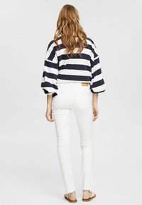 Námořnické a bílé pruhované oversized tričko s zvonovými rukávy, v kombinaci s úzkými bílými džíny a hnědými sandály, pohled zezadu.