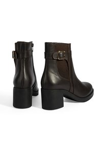 Bruine leren enkelboots met een textuur elastische paneel en een gespaccent. Stevige zwarte hak. Gladde afwerking en afgeronde neuzen.